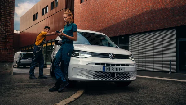 Volkswagen Caddy. En Man Och En Kvinna Lutar Sig Mot En Vit Transportbil.